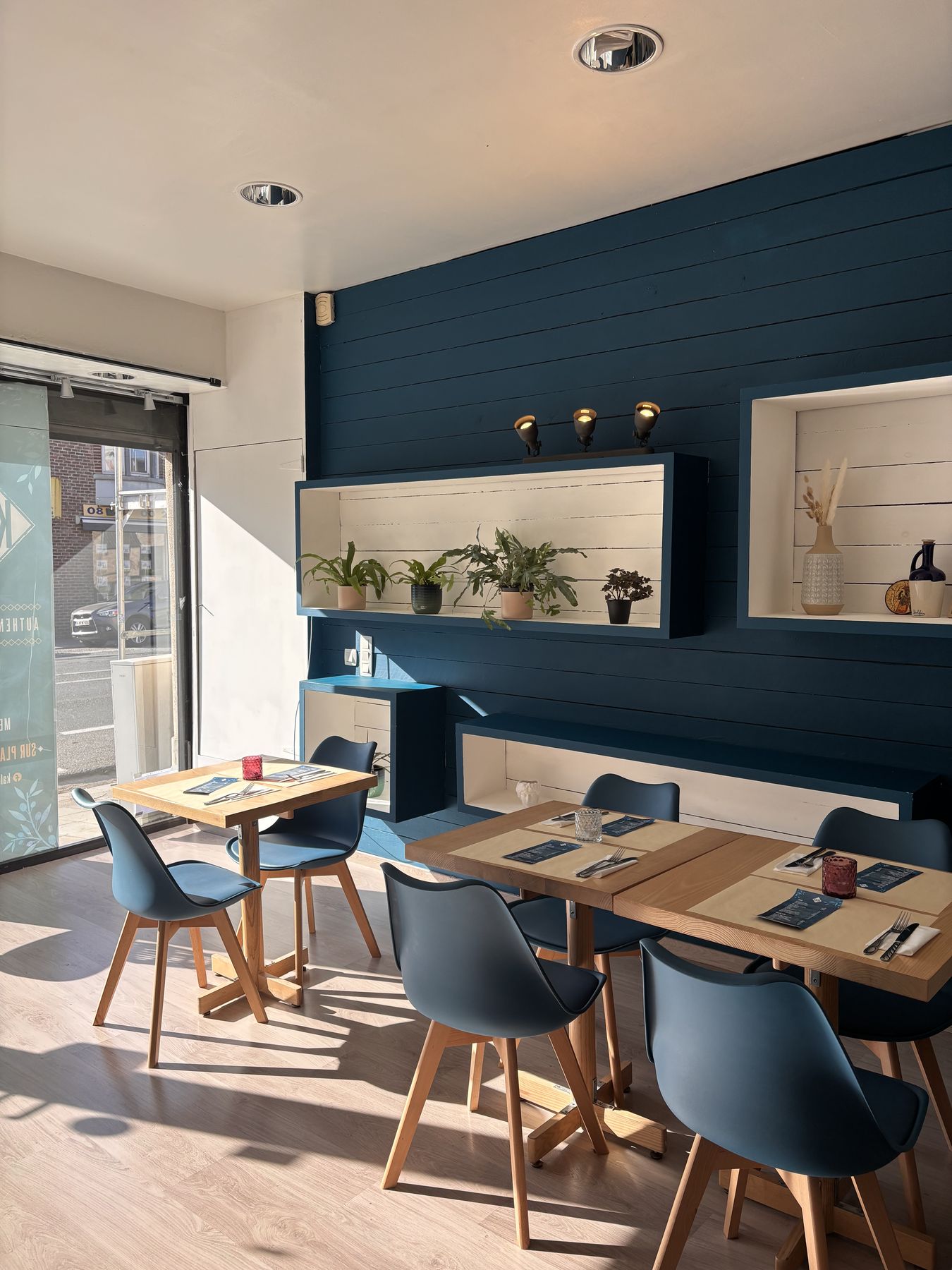 Mur bleu en lambris, tables en bois clair et chaises bleues
